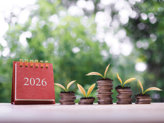 2026 desk calendar, Plants growing up on stack of coins. The concept of saving money, Financial, Investment and Business growing in new year 2026