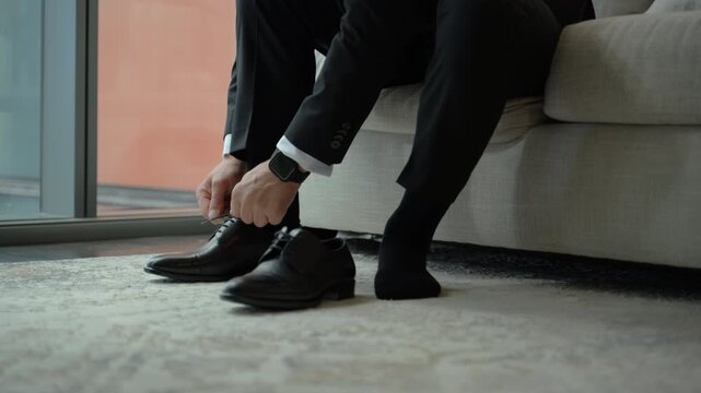 Groom tying the laces of his formal black shoes while getting ready, capturing a calm and elegant wedding preparation moment.