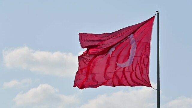 The red Turkish flag, hoisted on the flagpole, waves against the blue sky as a patriotic national symbol of a country fluttering in the wind.