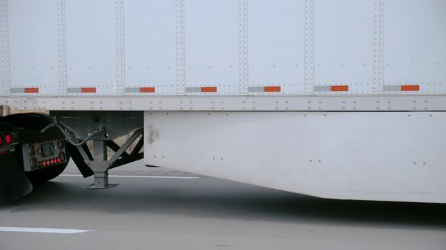 POV Close tracking shot of a semi-truck trailer and rear wheels moving on the road, showing suspension, landing gear, and transport details in motion