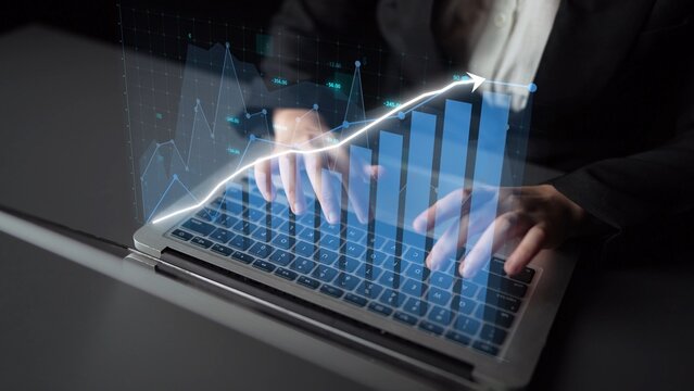 A business professional types on a laptop with digital graphs and data overlays illustrating financial growth and analysis, representing modern technology in the workplace. Copula - Powered by Adobe