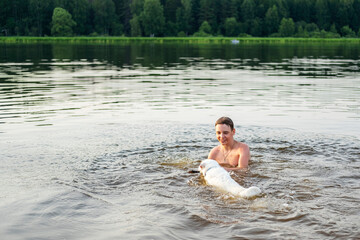 Fototapeta premium Person cheerfully enjoys swimming with their dog in a peaceful lake surrounded by lush greenery. The moment captures a sense of joy and companionship in a natural setting.
