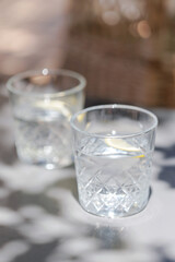 Two crystal glasses with lemon water in soft summer shadow