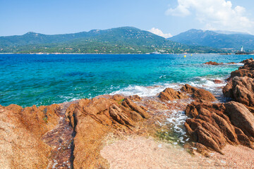 A vivid coastal scene with rugged rocks along a sandy beach and calm turquoise water
