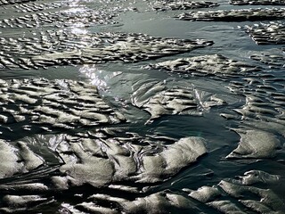 Low tide mudflat seascape with shimmering sunlight reflections on wet sand patterns and shallow tidal pools, tranquil coastal landscape texture background at the beach