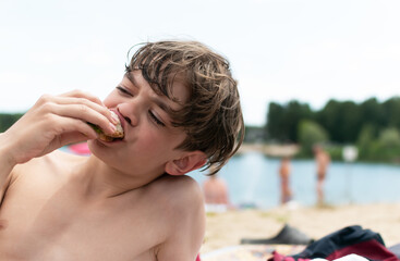 A little boy eats food on the beach after swimming