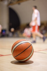 Ballon de basket sur un terrain int&eacute;rieur avec joueurs flous en arri&egrave;re-plan