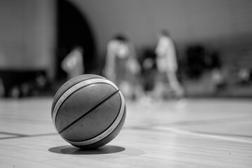 Ballon de basket sur un terrain int&eacute;rieur avec joueurs flous en arri&egrave;re-plan