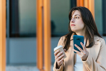 Businesswoman holding smartphone and coffee reflecting outdoors