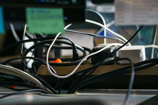 Tangled power cords, adapters, and chargers on desk symbolize cable clutter, technology overload, home office chaos, and workplace organization issues