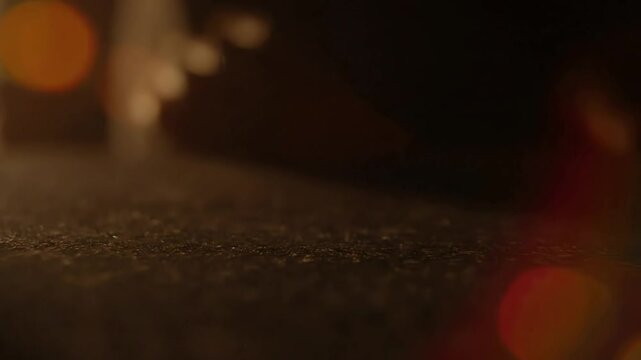 A cinematic macro shot of a hand wiping away dust from a dark textured surface with warm lens flare.