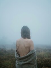 Frau mit R&uuml;cken zur Kamera mit einer Decke steht in einer Nebel Landschaft