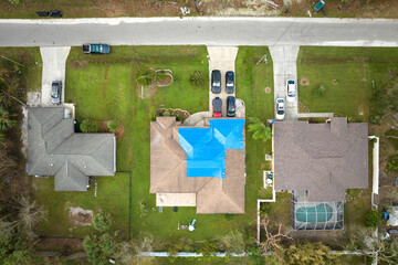 Top view of leaking house roof covered with protective tarp sheets against rain water leaks until replacement of asphalt shingles. Damage of building rooftop as aftermath of hurricane Ian in Florida