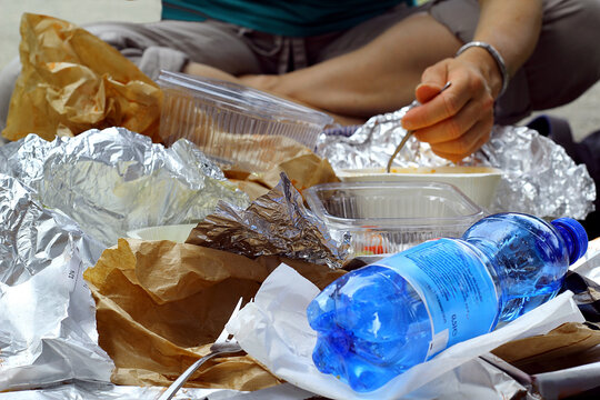 Eine Frau beim essen vor einem M&uuml;llberg aus Verpackungen.
