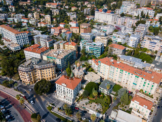 Drone shot of the historic Chiesa Russa in Sanremo, Italy. Scenic urban panorama featuring Mediterranean buildings, palm trees, and coastal road against a backdrop of misty Alps in Liguria