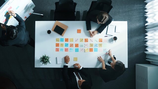 Top down aerial view of smart business people discuss and share marketing strategy while executive manager report sales and writing idea on whiteboard. Startup team working together. Directorate.
