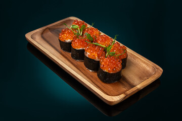 Sushi roll with red caviar and salmon on wooden plate, dark background
