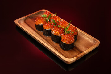 Sushi roll with red caviar and salmon on wooden plate, dark background with red backlight