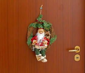 Christmas wreath hanging on closed brown entrance door with Santa Claus