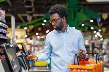 Man scanning groceries at a modern self-checkout terminal while using a smartphone for contactless payment or product info, showcasing quick, convenient digital retail shopping