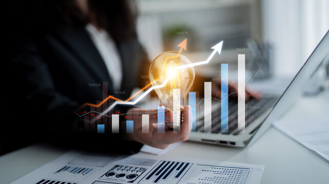 A professional business setting showcasing charts and financial reports with a laptop. A light bulb symbolizes innovation and growth, highlighting data-driven success. Scalp - Powered by Adobe