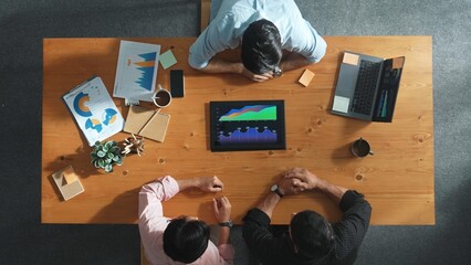 Top aerial view of business man present financial graph to group of smart investors. Professional male leader analyze graph and explain marketing idea by using tablet on meeting table. Convocation.