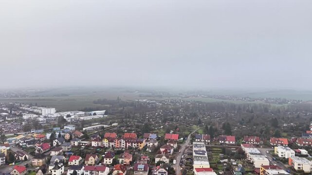 aerial view residential sprawl meeting open fields, low rise rooftops stretching to horizon, overcast sky,