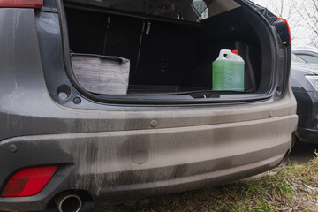 Plastic canister of car fluid standing in open trunk of dusty vehicle