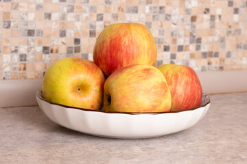 Plate with several fresh apples standing on a kitchen countertop