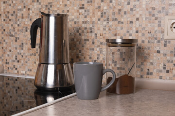 kitchen still life with moka pot, grey ceramic mug, and glass jar of ground coffee