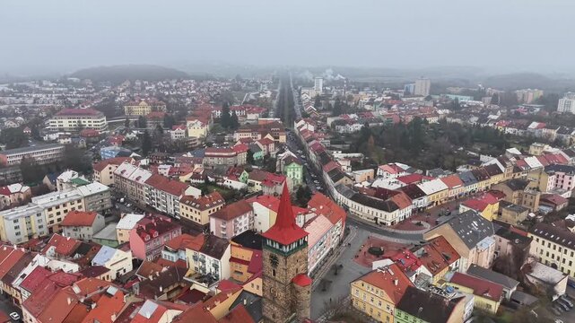aerial view church steeple and curved main street lined with colorful roofs, dense urban fabric, cloudy sky,