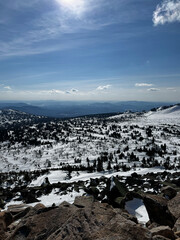 Winter mountain panorama with snow-covered forest and blue sky.