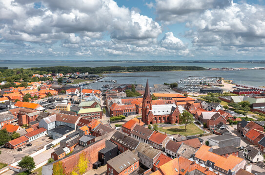 Aerial view of Nyk&oslash;bing Mors, North Jutland Region, Denmark&mdash;harbor cityscape and skyline with red-roofed houses, landmark church, marina, and Limfjord coastline under dramatic summer clouds