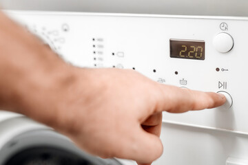 Close-up of a hand pressing the start button on a modern washing machine control panel, showcasing digital display and user-friendly design for efficient laundry management