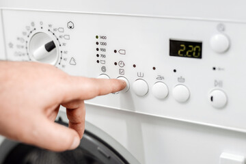Hand of a person adjusting settings on a modern washing machine control panel, showcasing various buttons and a digital display for laundry cycles and options