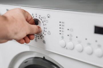 Hand adjusting settings on a modern washing machine with a sleek design, showcasing control knobs and digital display for efficient laundry management