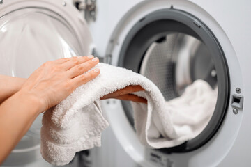 Hands of a woman holding a freshly laundered white towel, removing it from a modern washing machine, showcasing home laundry care and cleanliness in a bright environment