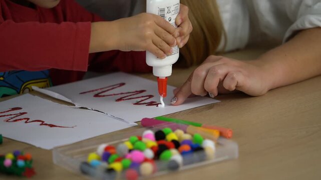 Child hands using glue for creative art project with mother