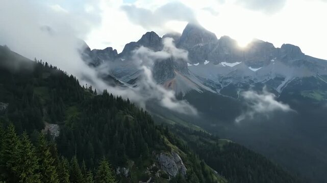 Misty mountain peaks shrouded in fog with sunbeams breaking through dramatic clouds and evergreen forest below