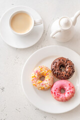 Trio of glazed donuts with coffee cup and pitcher in bright morning light