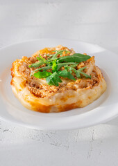 Circular lasagna presentation topped with fresh arugula served on elegant white plate