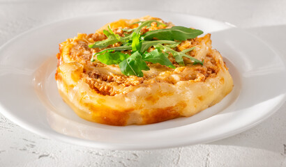 Circular lasagna presentation topped with fresh arugula served on elegant white plate