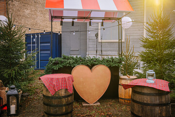 Festive outdoor market scene featuring a large heart-shaped decoration, surrounded by wooden barrels and decorated tables, creating a warm and inviting atmosphere for celebrations