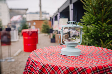 Vintage lantern placed on a red plaid tablecloth, surrounded by festive decorations and greenery, creating a cozy outdoor atmosphere for gatherings and celebrations