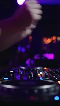 Close-up of DJ hands mixing electronic music on professional controller with colorful lights in a dark nightclub party atmosphere during live set