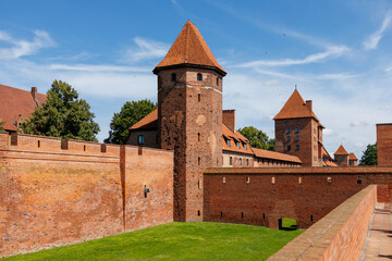 Brick defensive walls and towers of Malbork Castle with inner courtyard and green lawn under blue sky