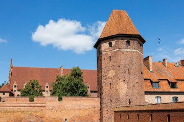 Close view of brick tower and fortified walls of Malbork Castle against blue sky