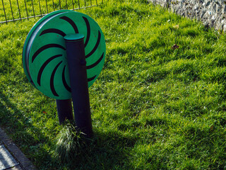 A green and black spinning object with a tree design on it is sitting in a grassy field. The object is surrounded by tall grass and he is a part of a game or activity
