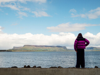 Teenager girl tourist is looking at amazing seascape with ocean and Benbulben flat top mountain in the background with blue cloudy sky, travel and tourism in Ireland. Sligo area.