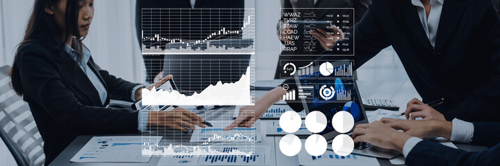 Professionals engaged in a business meeting analyze financial data using graphs and charts displayed on screens, promoting collaboration and strategic planning. Axiom